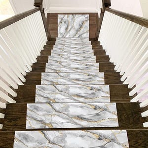 Può includere: Scala con gradini con motivo marmorizzato. I gradini presentano un design grigio, bianco e oro, creando un aspetto lussuoso. La scala è in legno scuro e la ringhiera è bianca.