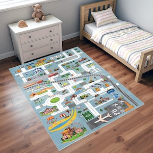Può includere: Un tappeto gioco azzurro per bambini con un design a mappa stradale. Il tappeto presenta strade, edifici e vari veicoli. È visibile un aeroporto con pista e aereo. Il tappeto è posato su un pavimento in legno.