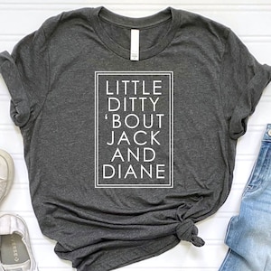 May include: A dark grey t-shirt with the text "LITTLE DITTY 'BOUT JACK AND DIANE" printed in white inside a white rectangle. The t-shirt is paired with light blue jeans and white sneakers.