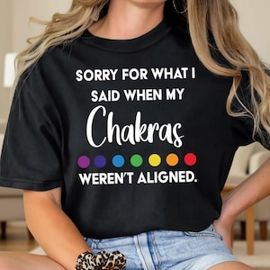 May include: Black t-shirt with the text "SORRY FOR WHAT I SAID WHEN MY Chakras WEREN'T ALIGNED." The word "Chakras" is in a cursive font, and below it are seven colored circles in a rainbow pattern. The shirt is a casual style.