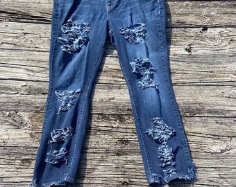 May include: Distressed blue denim jeans with several rips and tears throughout the fabric. The jeans have a straight leg fit and a mid-rise waist.