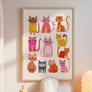 May include: A framed print featuring colorful cartoon cats in various poses. The artwork includes cats in shades of yellow, pink, orange, and blue. A wooden stacking toy, a cloud-shaped pillow, and a textured lamp sit on a white dresser.