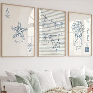 May include: Three framed art prints with a coastal theme. The prints feature blue line drawings of a starfish, lingerie on a clothesline, and a seashell. The starfish print includes the text "Bonjour le mer".