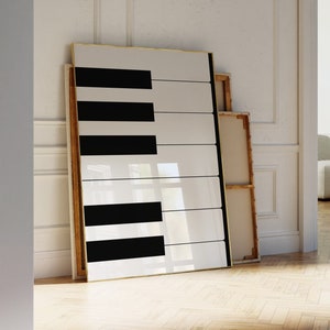 以下が含まれることがあります： 白黒のピアノの鍵盤が描かれた大きな額縁付きのプリント。プリントは壁にもたれており、金色の額縁が付いている。