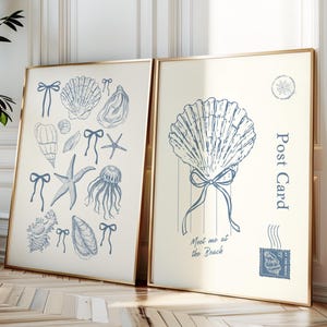 Könnte beinhalten: Zwei gerahmte Kunstdrucke mit goldenen Rahmen. Der linke Druck zeigt blaue Illustrationen von Muscheln, Seesternen und Quallen mit Schleifen. Der rechte Druck hat eine große Muschelillustration mit dem Text "Post Card" und "Meet me at the Beach".