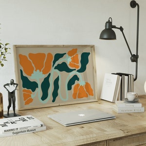 Pu&ograve; includere: Una stampa incorniciata di un design floreale astratto con colori arancio, verde acqua e blu chiaro. La stampa &egrave; appesa a un muro sopra una scrivania con un laptop, libri e una lampada.