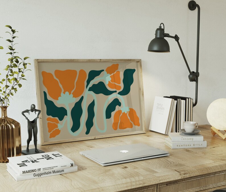 Pu&ograve; includere: Una stampa incorniciata di un design floreale astratto con colori arancio, verde acqua e blu chiaro. La stampa &egrave; appesa a un muro sopra una scrivania con un laptop, libri e una lampada.