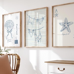 May include: Three framed art prints with a coastal theme. The prints feature blue line drawings of a seashell, lingerie hanging on a clothesline, and a starfish with playing card symbols. The frames are light brown.