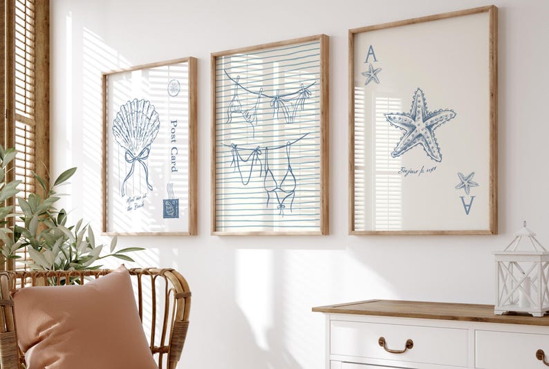 May include: Three framed art prints with a coastal theme. The prints feature blue line drawings of a seashell, lingerie hanging on a clothesline, and a starfish with playing card symbols. The frames are light brown.