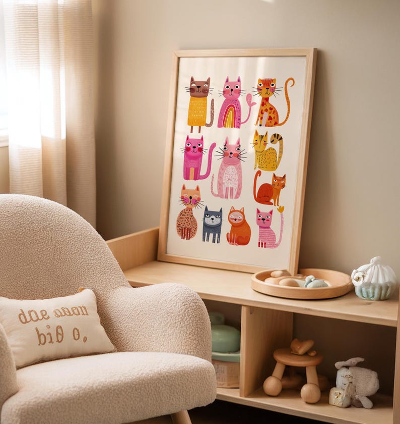 May include: A framed art print featuring colorful cat illustrations. The cats are depicted in various poses and colors, including orange, pink, and brown, with whimsical details. The artwork is displayed in a light-colored wooden frame.