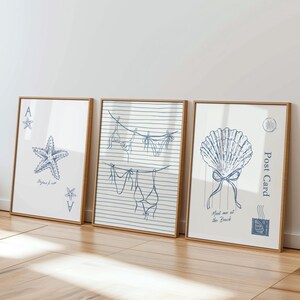 May include: Three framed art prints with beach-themed illustrations. One features a starfish and playing card symbols, another shows a clothesline with swimwear, and the last depicts a seashell with text that reads "Meet me at the Beach."