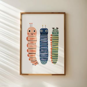 May include: A framed art print featuring three whimsical caterpillar illustrations. The caterpillars are in shades of pink, blue, and green, with striped bodies and smiling faces. The artwork is set against a white background.