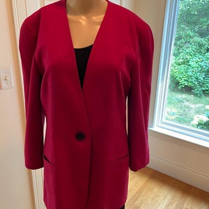 May include: A magenta blazer with a single button closure and two pockets. The blazer has a v-neck and long sleeves.