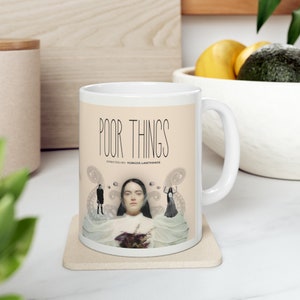 May include: White ceramic mug with a graphic of a woman in a white dress and the text "Poor Things" with the words "Directed by Yorgos Lanthimos" below.
