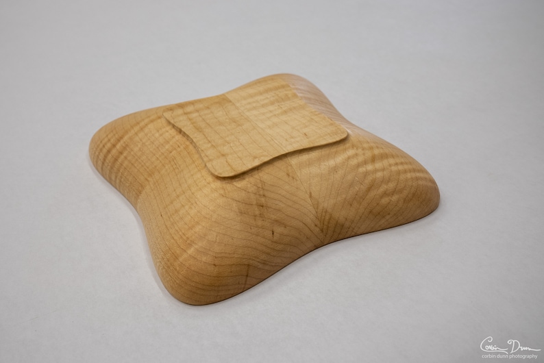 May include: A light wood bowl with a square-shaped bottom. The bowl is made of maple wood and has a natural wood finish.