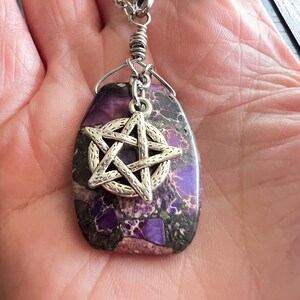 May include: A purple and black stone pendant with a silver pentagram charm. The pendant is on a silver chain. The stone has a unique pattern and is an oval shape.