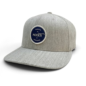 以下が含まれることがあります： グレーと白のベースボールキャップに、ネイビーブルーの円形のワッペンが付いています。ワッペンには「Handcrafted NC Noceti Custom Guitars」と書いてあります。