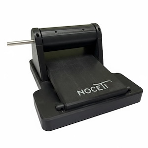 Puede incluir: Una máquina para hacer pasta negra con un mango plateado. La máquina tiene una base plana y un mecanismo de rodillos. La palabra "NOCETT" está impresa en la parte delantera. Dimensiones en centímetros.