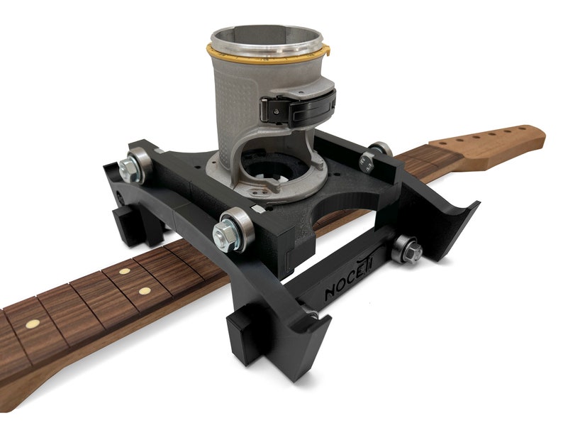 Puede incluir: Un jig de enrutador negro con una base de enrutador plateada y un m&aacute;stil de guitarra de madera. El jig est&aacute; etiquetado como "NOCETI".