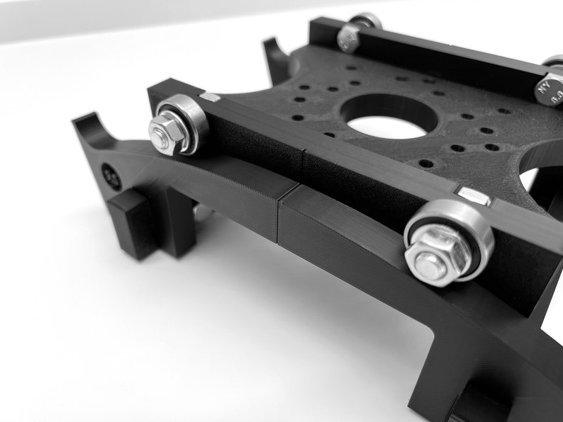 Puede incluir: Una plataforma negra impresa en 3D con cuatro ruedas y un agujero central. La plataforma est&aacute; dise&ntilde;ada para ser utilizada con una impresora 3D.