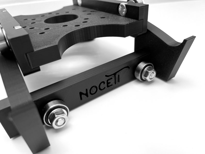 Puede incluir: Un deslizador de c&aacute;mara negro impreso en 3D con la palabra "NOCETI" grabada en el lateral. El deslizador tiene dos rodamientos met&aacute;licos y un tornillo met&aacute;lico a cada lado.