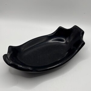 May include: A glossy black serving dish with a unique, elongated shape. The dish has gently curved sides and a slightly raised, decorative edge. The overall design is simple yet elegant, suitable for serving appetizers or small portions.