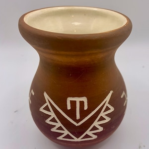May include: A small, brown ceramic vase with a white geometric design. The vase has a rounded body and a flared lip.