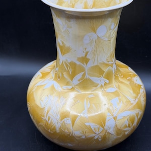May include: A decorative vase with a bulbous base and flared rim. The vase is primarily yellow with a white, crystalline pattern. The interior rim is white. The vase is likely ceramic or glass.