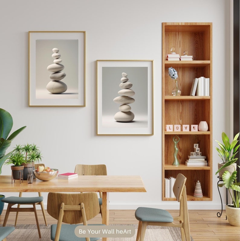 Puede incluir: Dos impresiones enmarcadas de piedras blancas apiladas sobre un fondo gris claro. Las impresiones est&aacute;n colgadas en una pared blanca sobre una mesa de comedor de madera con cuatro sillas. Una estanter&iacute;a de madera con estantes llenos de libros, objetos decorativos y un peque&ntilde;o jarr&oacute;n con flores azules se encuentra a la derecha de la imagen. El texto "Be Your Wall heArt" est&aacute; en la parte inferior de la imagen.