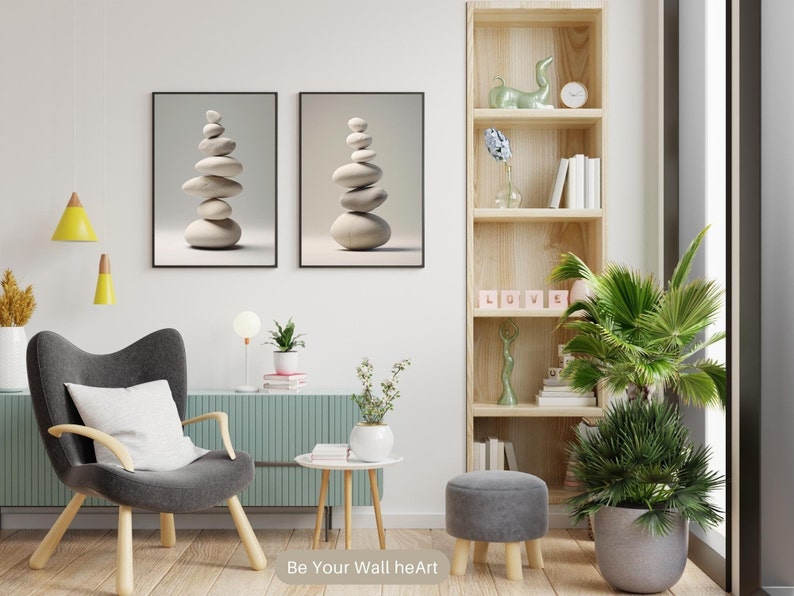 Puede incluir: Dos impresiones enmarcadas de piedras blancas apiladas sobre un fondo beige claro. Las impresiones est&aacute;n colgadas en una pared blanca sobre un sill&oacute;n gris con un coj&iacute;n blanco. Una estanter&iacute;a de madera con una escultura de cer&aacute;mica verde, libros y un reloj se encuentra a la derecha de la imagen. Una planta verde en maceta se encuentra en la esquina de la habitaci&oacute;n.