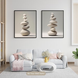 Puede incluir: Dos impresiones enmarcadas de piedras blancas apiladas sobre un fondo blanco. Las impresiones est&aacute;n colgadas en una pared blanca sobre un sof&aacute; gris claro con almohadas de color rosa y gris. Un jarr&oacute;n amarillo con flores blancas se encuentra sobre una mesa de caf&eacute; ovalada blanca.