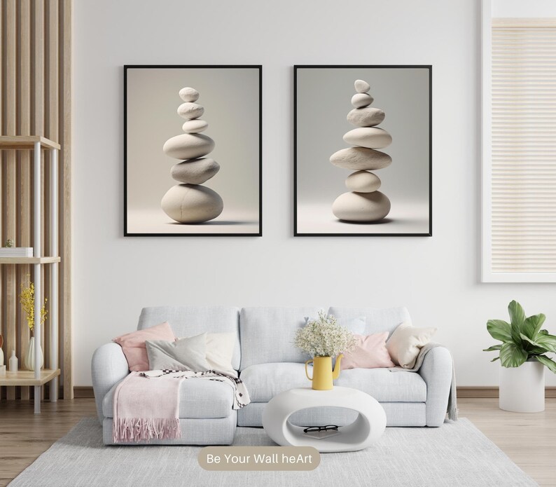 Puede incluir: Dos impresiones enmarcadas de piedras blancas apiladas sobre un fondo blanco. Las impresiones est&aacute;n colgadas en una pared blanca sobre un sof&aacute; gris claro con almohadas de color rosa y gris. Un jarr&oacute;n amarillo con flores blancas se encuentra sobre una mesa de caf&eacute; ovalada blanca.