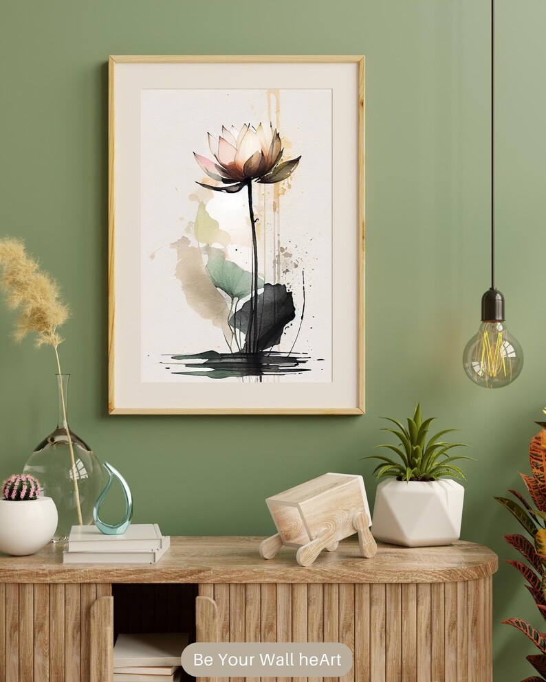 May include: A watercolor painting of a pink lotus flower with green leaves and a brown stem. The painting is framed in a light wood frame and is hanging on a green wall. The painting is surrounded by a variety of home decor items, including a vase with dried flowers, a cactus, a wooden sculpture, and a potted plant.