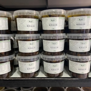 May include: A shelf stocked with multiple clear plastic containers filled with a dark brown liquid. Each container has a white label with the text "KBF KHALIE" printed on it.