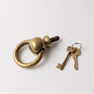 May include: A brass door knob with a round handle and a keyhole. The knob is attached to a metal ring.
