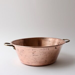 May include: A copper bowl with two brass handles. The bowl has a hammered finish and is slightly dented.