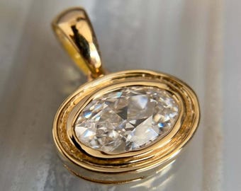 May include: A gold pendant featuring an oval-shaped, clear gemstone. The gemstone is set within a gold bezel, and the pendant has a simple, elegant design. The pendant is likely a piece of jewelry, such as a necklace.