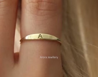 May include: A gold band ring with the letter "A" engraved on it. The ring is worn on a finger.