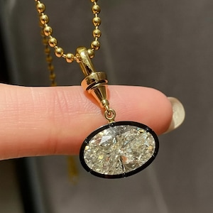 Può includere: Una collana con pendente in oro con un diamante ovale e un bordo nero. Il diamante è incastonato in una montatura d'oro e pende da una delicata catena d'oro.