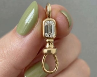 May include: A gold swivel clasp pendant featuring a rectangular emerald-cut clear gemstone set in a bezel frame. The metal component has a polished finish with a top loop for attachment and a rotating bottom ring mechanism for securing jewelry items.