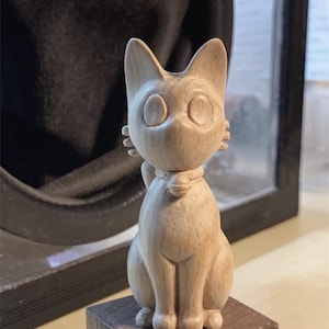 Puede incluir: Una figurita de gato de madera tallada a mano con un collar blanco. El gato está sentado erguido con las orejas levantadas y los ojos bien abiertos. La figurita está hecha de madera de color claro y tiene un acabado liso y pulido.