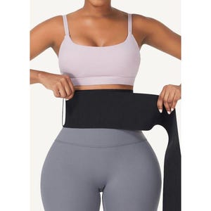 May include: A black waist trainer with a wide band and long straps. The trainer is worn over a light purple sports bra and gray leggings.