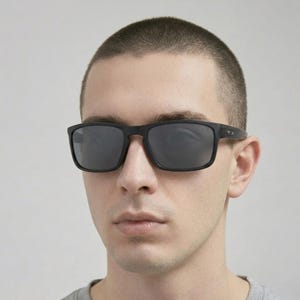 Puede incluir: Gafas de sol negras de montura cuadrada con lentes oscuras. Las gafas de sol tienen un acabado mate. Las monturas son gruesas y las lentes reflectantes. El estilo es moderno y minimalista.