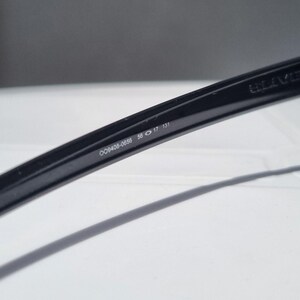 Puede incluir: Primer plano de una montura de gafas negra con el n&uacute;mero de modelo OO9408-0655, un ancho de lente de 56 mm, un ancho de puente de 17 mm y una longitud de patilla de 131 mm. La montura es de material negro brillante.