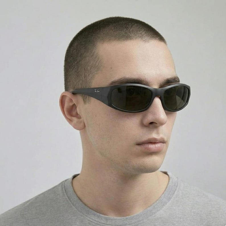 May include: Black wrap-around sunglasses with dark tinted lenses and a matte finish frame. The temples feature the Ray-Ban logo in small white lettering. The design provides full coverage around the eyes with a curved, aerodynamic shape.