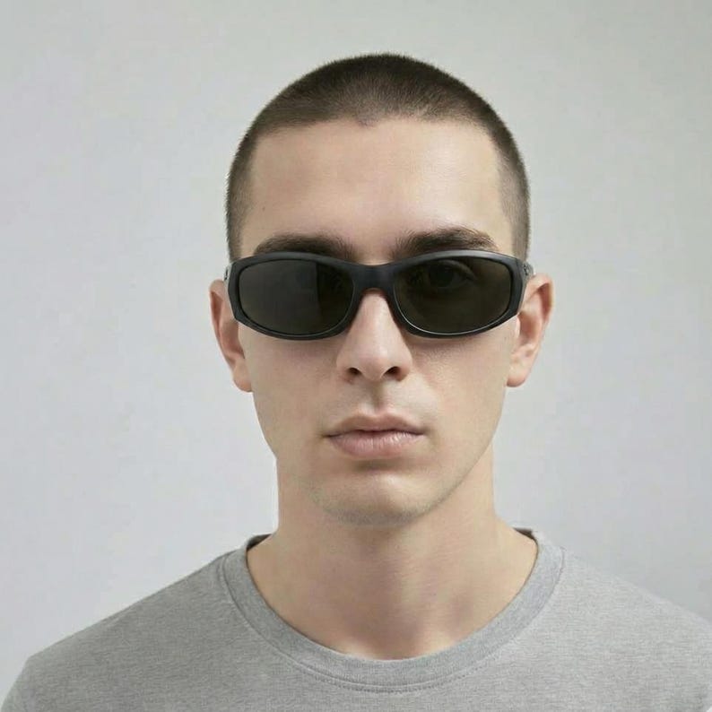May include: Black sunglasses featuring a wrap-around frame design with dark, tinted lenses. The eyewear has a smooth, matte black finish on the temples and bridge, providing a streamlined look that contours to the face for full coverage.