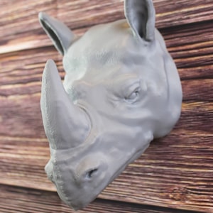 Può includere: Una scultura di testa di rinoceronte grigia con una texture dettagliata. La scultura è montata su una parete di legno.