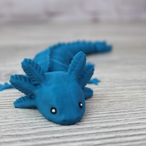 May include: A blue 3D printed axolotl figurine with white eyes. The figurine is posed with its head facing forward and its tail curled behind it.