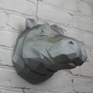 May include: A gray, geometric, 3D printed hippopotamus head wall sculpture. The sculpture is made of a textured, polyhedral material and has a realistic, detailed design.