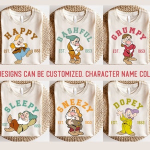 Puede incluir: Ocho diseños diferentes de camisetas con los siete enanitos de Blancanieves y los Siete Enanitos. Cada diseño presenta un enanito diferente con su nombre en una fuente de estilo universitario vintage y el texto "EST. 1953".